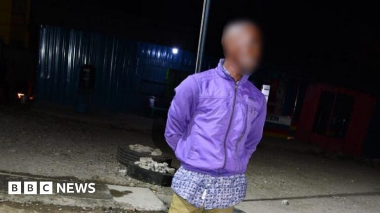 A man, with his face blurred, is pictured at night time wearing a purple jacket and khaki trousers.