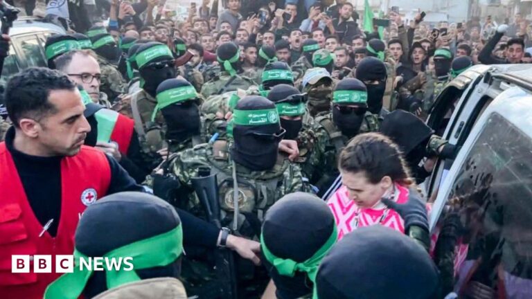 One of the three Israeli hostages released on Sunday in Gaza is handed over by Hamas fighters to a member of the Red Cross.
