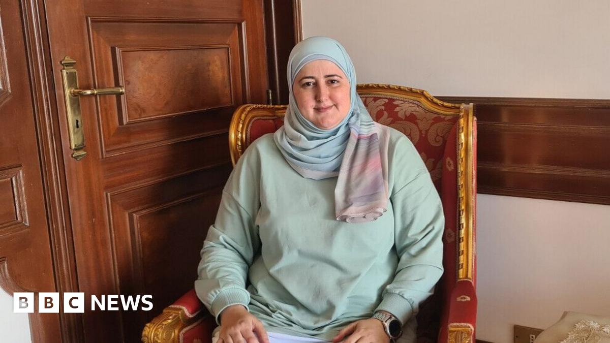 Hania is sitting in a chair, smiling at the camera. She is wearing a pastel green top and a pastel blue headscarf.