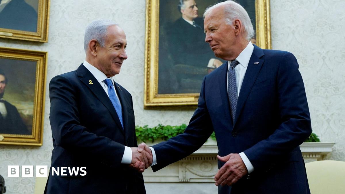 Benjamin Netanyahu sits with his hands on his knees in the oval office, wearing a blue tight and dark suit. Joe Biden sits to his left, wearing a navy suit with clasped hands.