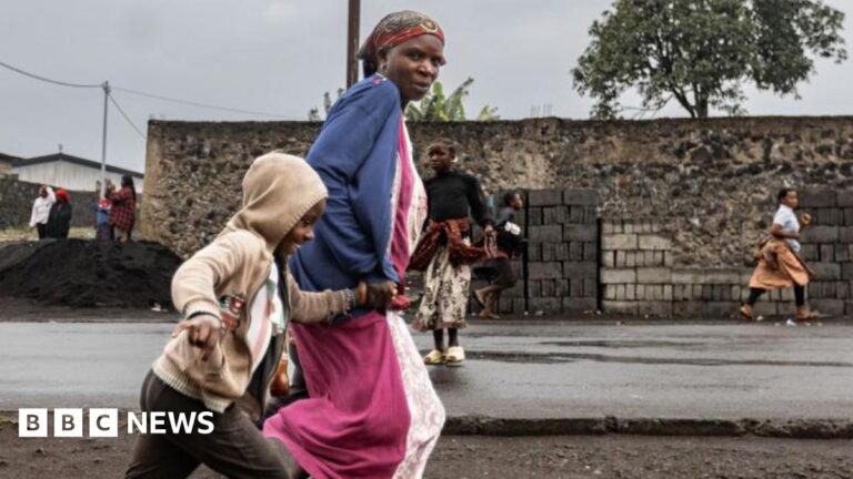 A woman in a pink dress and blue top and child run on a street in Goma