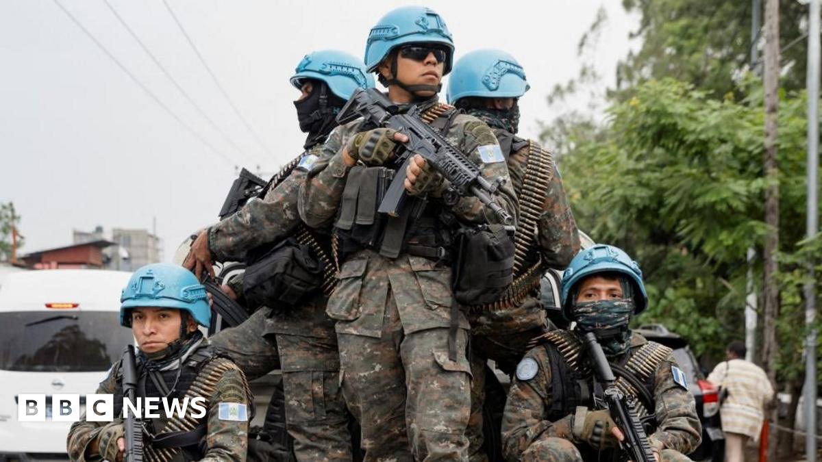 Five soldiers wearing blue hats stand on the back of a truck in front of trees in Goma, DR Congo.