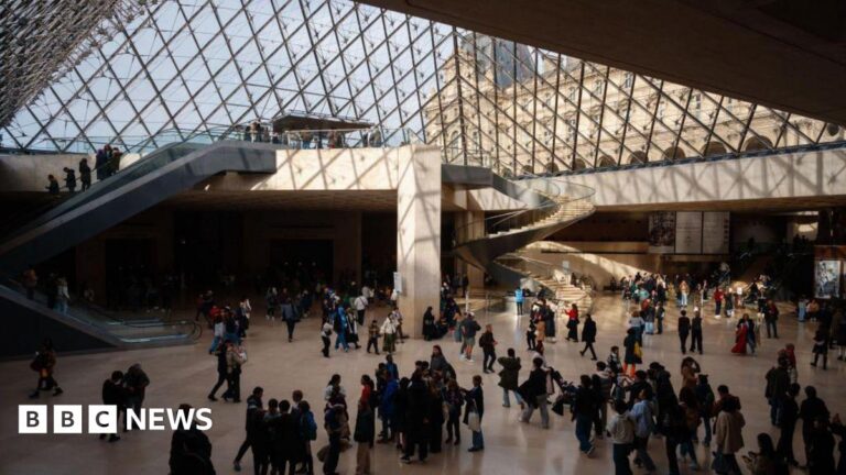 A view of the hall of the Louvre under the glass pyramid with lots of people