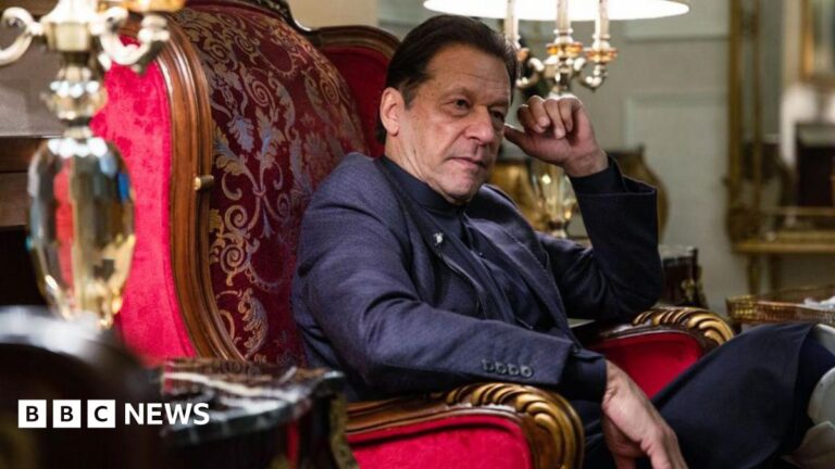 Side view of Imran Khan as he sits on a red velvet armchair, his hands on the arm rests
