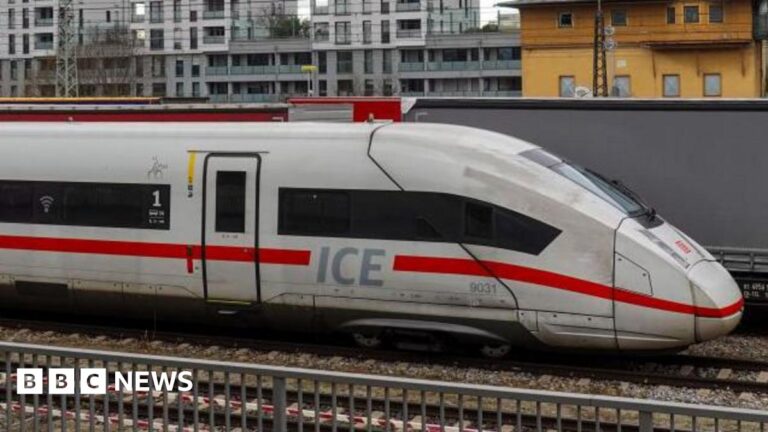 Front end of a German ICE train, travelling from left to right. Buildings can be seen in the background.