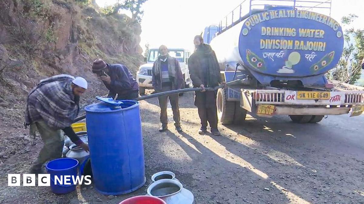 People wearing caps and mufflers fill water in their buckets and drums from a public water tanker in the Rajouri district.