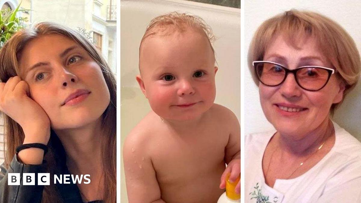 A lady with short blonde hair looks into the camera. Behind her is her apartment which has been totally demolished by a bomb.