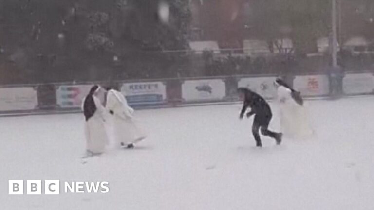 Three nuns in white clothing and black headdress in a snowball fight with a priest dressed in black.