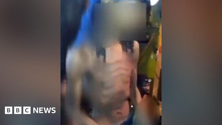 A screengrab shows an emaciated illegal miner with his shirt off in an underground tunnel. The young man, with long hair, is captured in the dimly-lit passage alongside his fellow miners.