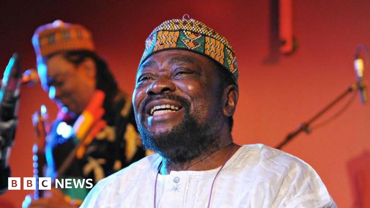 Teddy Osei, dressed in a crisp white linen shirt and a traditional African cap, radiates joy with a broad smile as he performs with his band Osibisa at the Front Room of the Queen Elizabeth Hall in 2010.