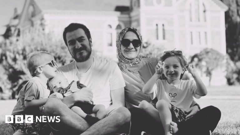Zehra Gültekin and her husband Bilal Gültekin smile in a black and white photo seated with their children on a lawn in front of a large building. Zehra is wearing a headscarf and dark glasses, and one child - on the far left of the picture - is also wearing sunglasses