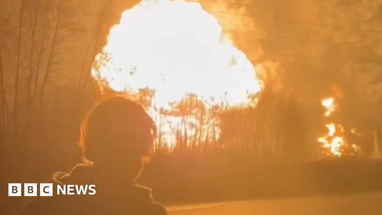 A man stands in the foreground as a fireball erupts at the Ryazan oil refinery