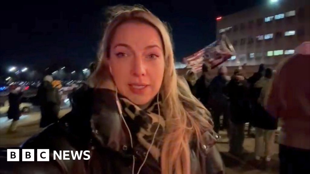 Emma Vardy is seen in a close-up at night with people behind her.