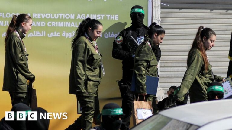 Four female Israeli soldiers in army uniform walking in a line, behind them is an armed Hamas fighter